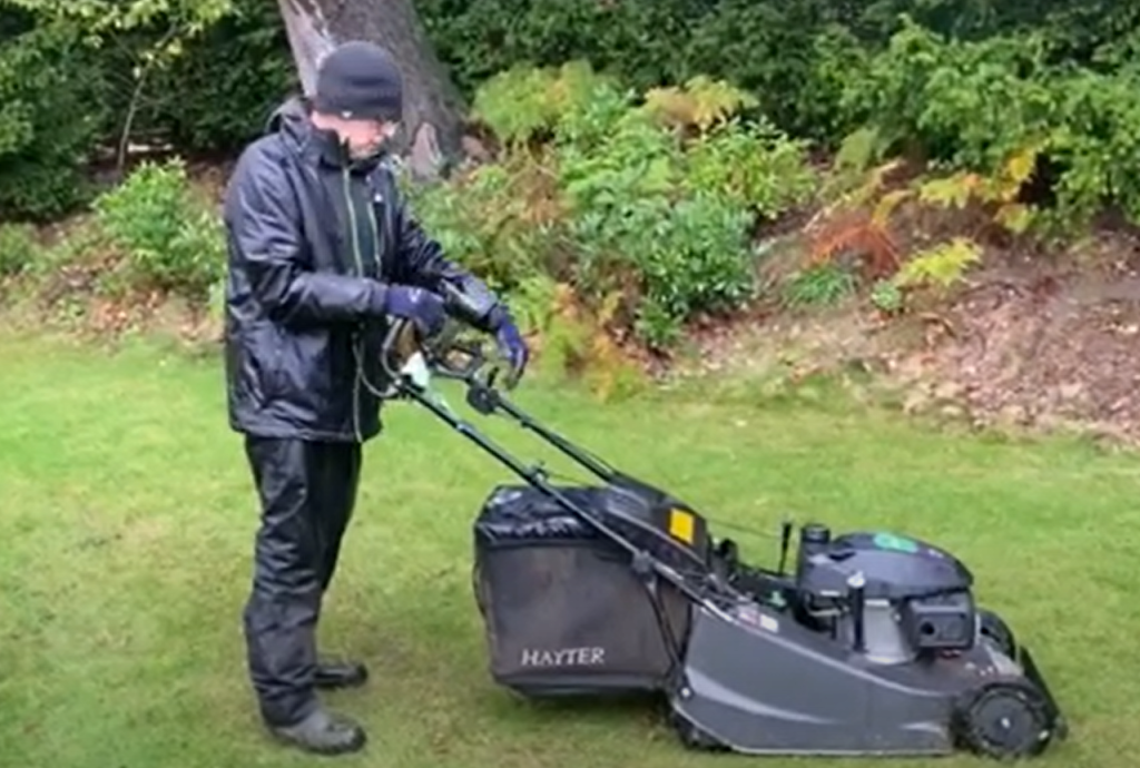 Ken in wet weather gear with a Hayter mower cutting a lawn.