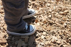 A pair of feet standing on a wood chip mulch.