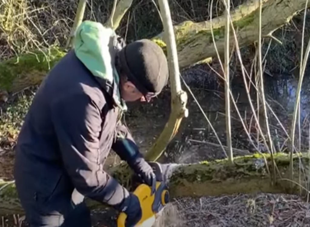 Ken using a Stiga chainsaw to cut down a tree trunk.