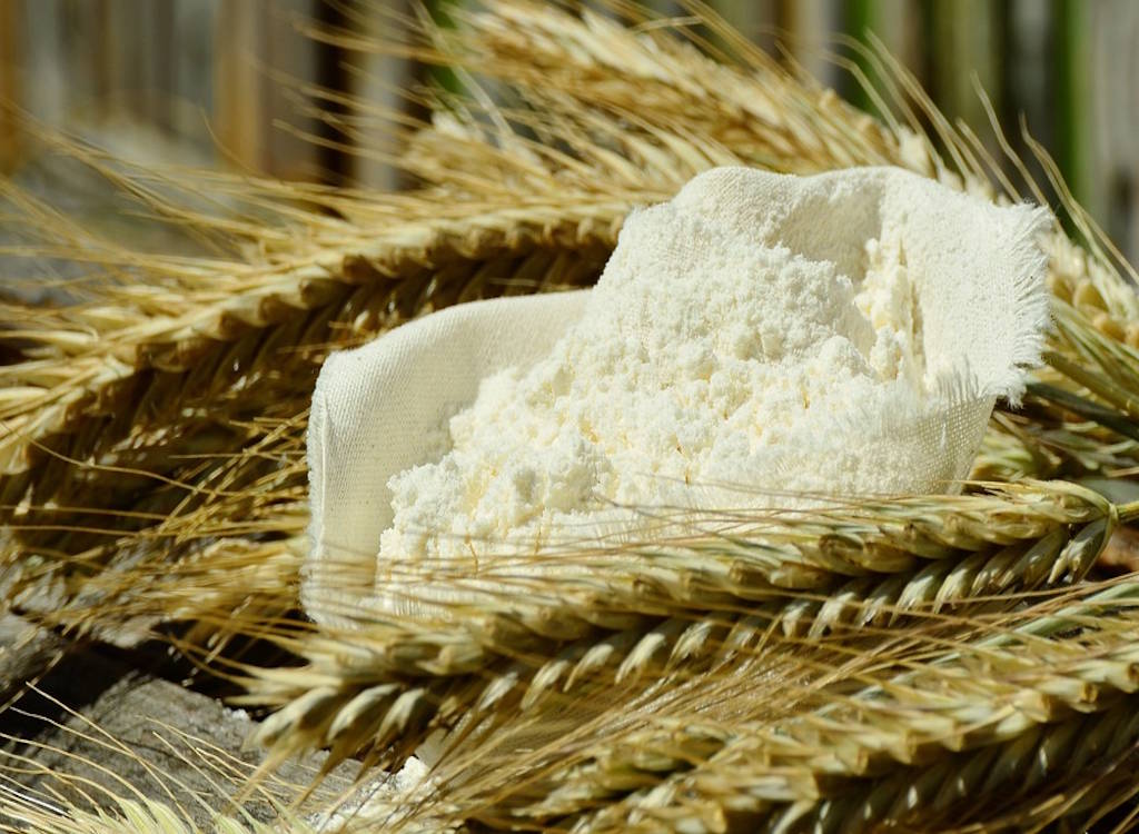 Ears of wheat and milled flour on a table top.